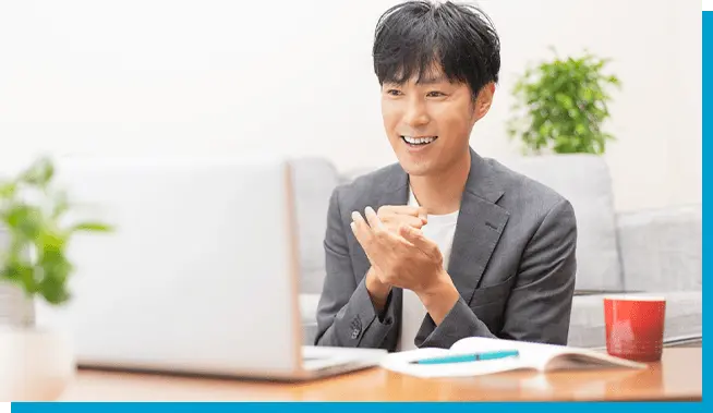 スーツ姿の男性がノートパソコンの前で笑顔を見せながらオンラインミーティングをしている様子
